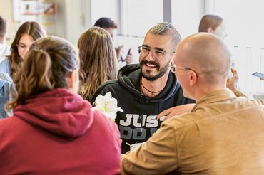 Mehrere Studierende sitzen in der Cafeteria an einem Tisch zusammen und reden.