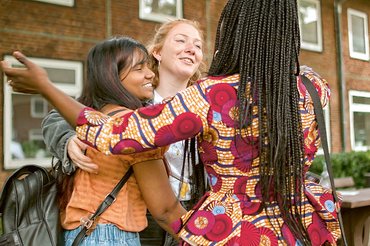 Drei Studentinnen umarmen sich. Sie haben unterschiedliche Hautfarben.