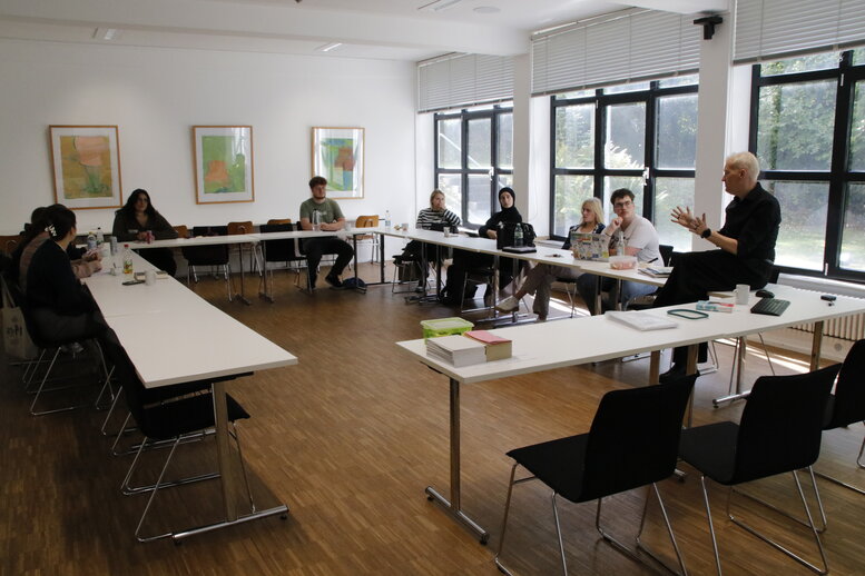 Im Seminarraum sitzen die Teilnehmenden an Tischen 