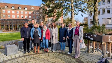 Eine Tagungsgruppe steht bei Sonnenschein zusammen im katho-Garten in Paderborn und ist fröhlich.