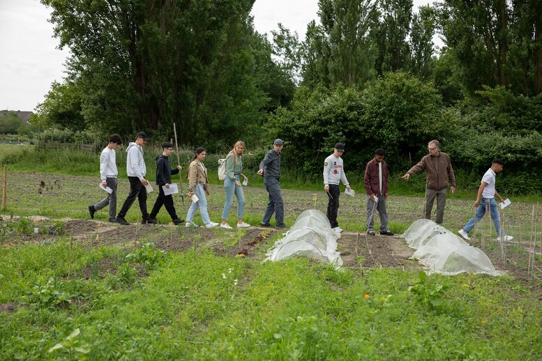 Eine Gruppe geht durch einen Garten und schaut sich diesen an. Zwei Personen der Gruppe zeigen auf eins der Beete.