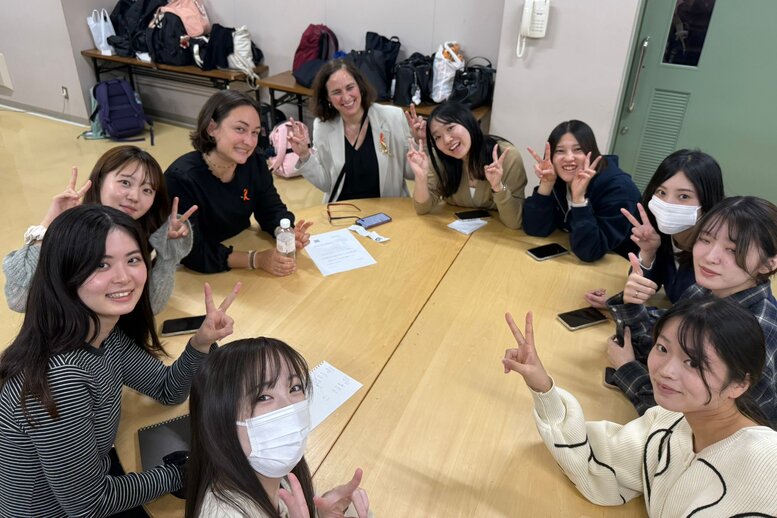 Eine Gruppe japanischer Studierender sitzen mit Rektorin an einem runden Tisch und lächeln in die Kamera.