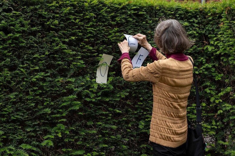 Eine Person hängt Buchstaben an einer Hecke auf.