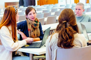 Studierende sitzen mit einer Dozentin an einem Tisch und reden miteinander.