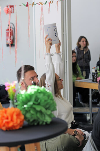 Ein Frau hält einen Zettel hoch auf dem eine 8 steht.