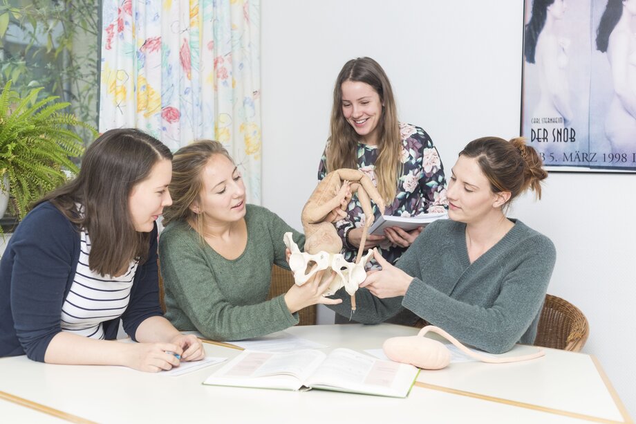 Vier Frauen üben an einem Modell Aufgaben aus der Hebammenkunde.