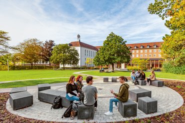 Studierende sitzen auf Steinquadern im Grünen vor der Paderborner katho.