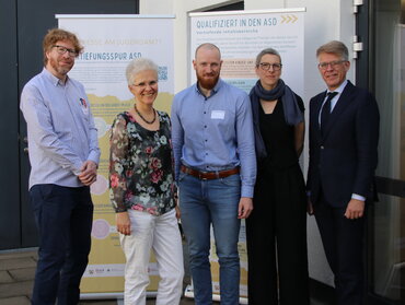 Alle Personen stehen vor einem Roll up der Vertiefungsspur im Innenhof