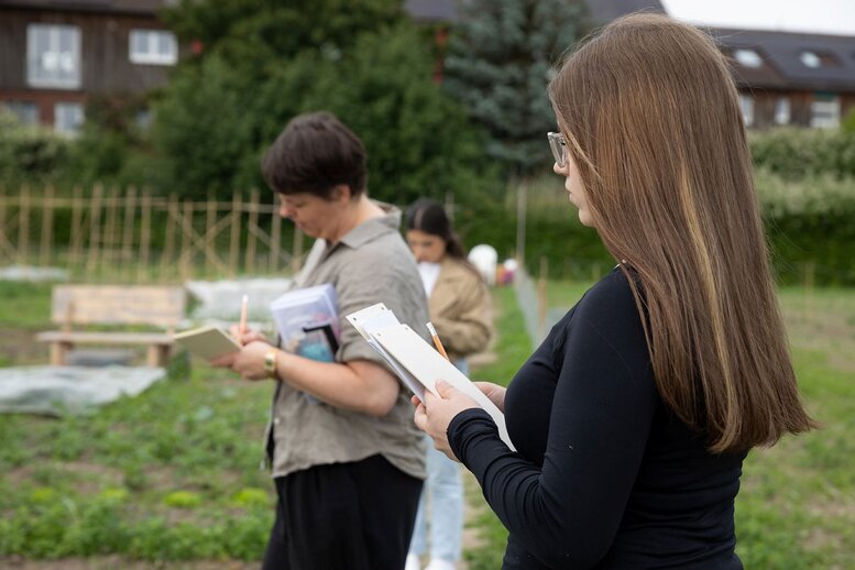 Drei Personen zeichnen in einen Garten.