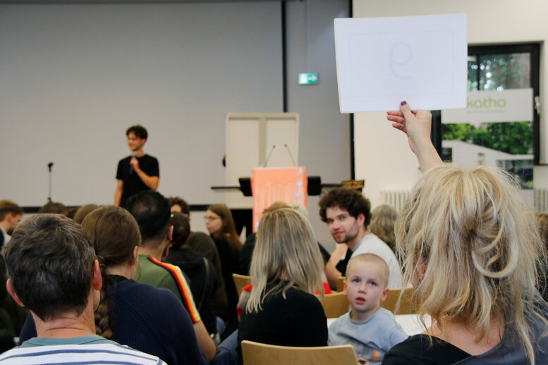 Eine Person hält einen Zettel mit einer Zahl drauf hoch. 