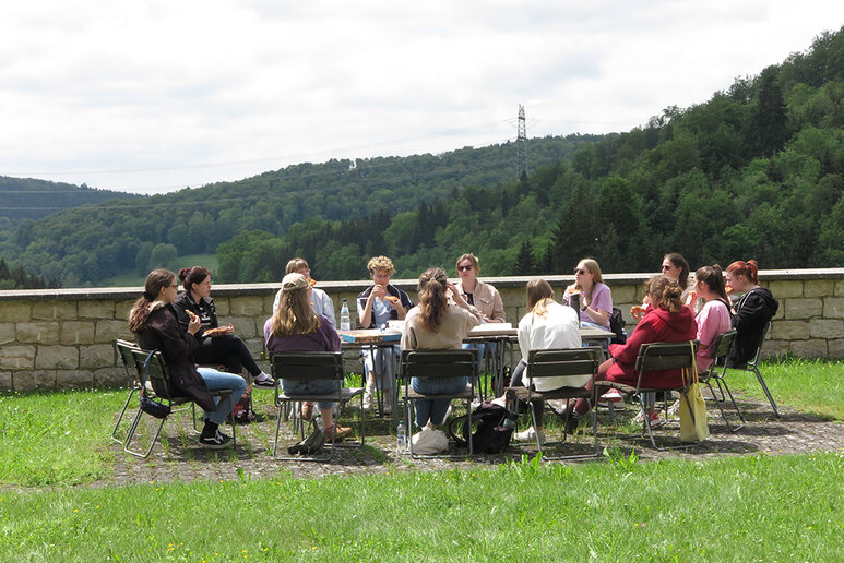 Eine Gruppe Menschen sitzt bei gutem Wetter gemeinsam draußen an einem Tisch.