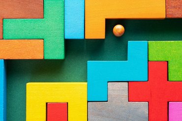 Labyrinth aus bunten Holzblöcken. Ein Weg ist zu erkennen in dem sich ein kleiner Ball befindet.