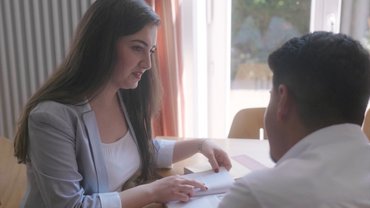 Ein Studentin erklärt jemand anderem etwas. Beide sitzen an einem Tisch in der Bibliothek Münster.
