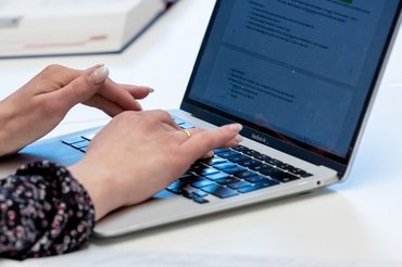 Die Hände einer Person die Notizen auf einem Laptop eintippt.